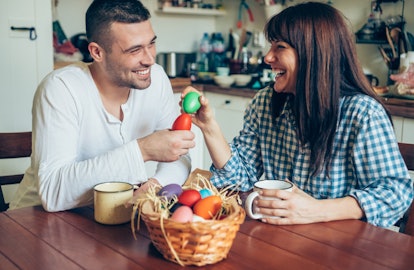 A young couple smiles at each other while holding their painted Easter eggs.