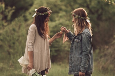 Two friends in flower crowns hold up Easter eggs in a field on a sunny day.