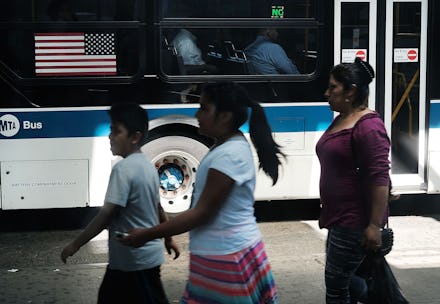 Latino citizens walking next to a bus with the flag of the U.S.A. on it