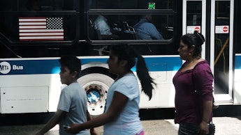 Latino citizens walking next to a bus with the flag of the U.S.A. on it
