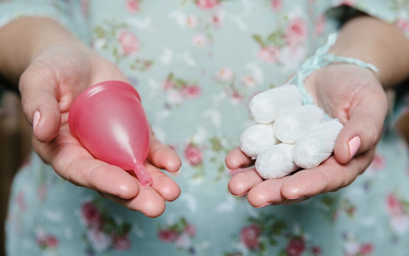 A woman holds a menstrual cup and a bunch of tampons. These reasons your period could be late are li...