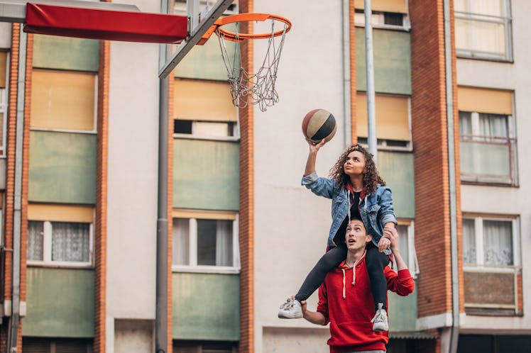 A young couple plays basketball outside of their colorful apartment building.