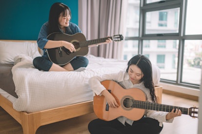 Two women play guitar in their apartment. Music and other art forms can be therapeutic. 