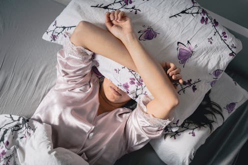 A woman with a pillow over her face struggles to fall back asleep after waking up in the middle of t...