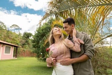 A young couple stands next to a palm tree in their front yard on a spring day.