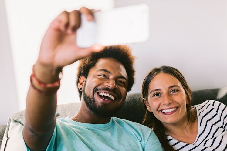 A young couple records a live video on Instagram on their phone, while sitting on their couch.