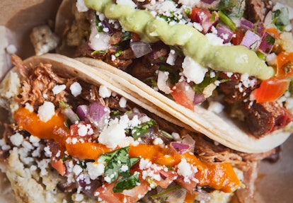 Two tacos are filled with cheese, meat, vegetables, and a tangy sauce.