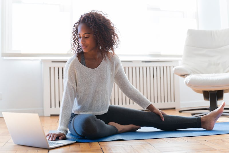 A woman stretches while watching a yoga with adriene video on youtube that's less than 30 minutes lo...