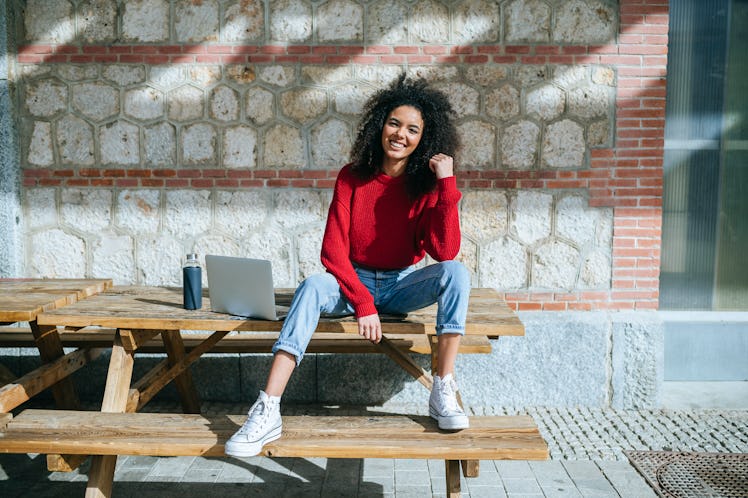 A young woman sits on a picnic table with her laptop and a resuable water bottle.