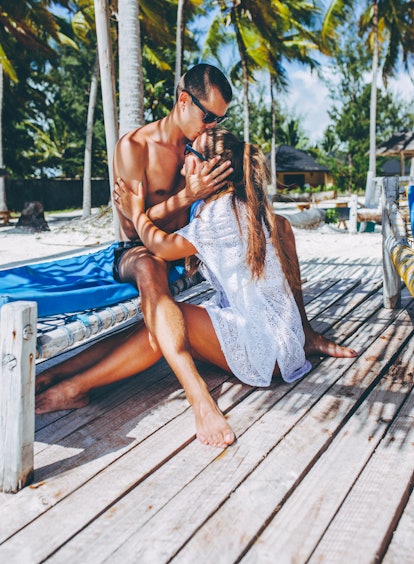 A young couple embraces while sitting on a lounge chair on the beach.