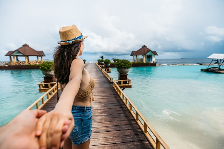 A young woman walks down an island's boardwalk while holding her partner's hand.