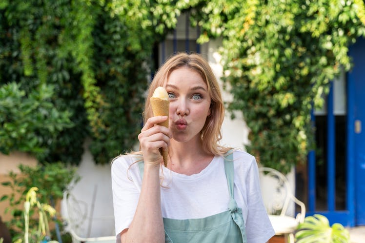 A young blonde woman poses with an ice cream cone in her backyard.