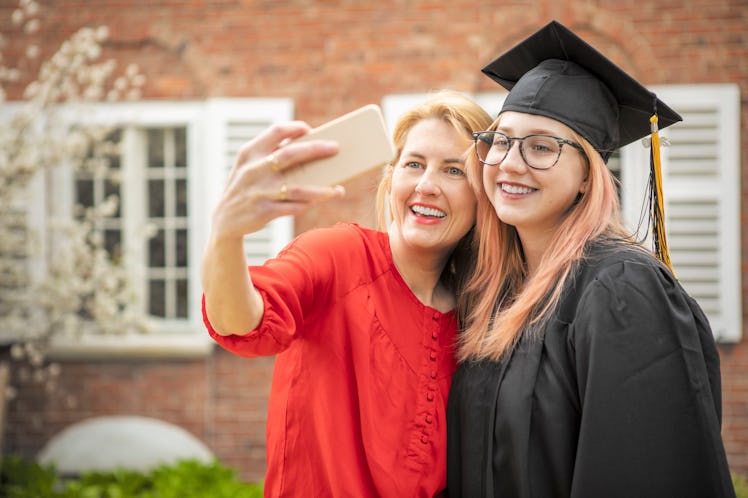 A mom takes a selfie with her daughter, who is wearing her graduation cap and gown. 