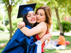 A happy graduate hugs her sister while wearing her cap and gown. 