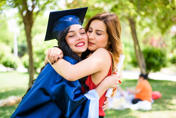A happy graduate hugs her sister while wearing her cap and gown.