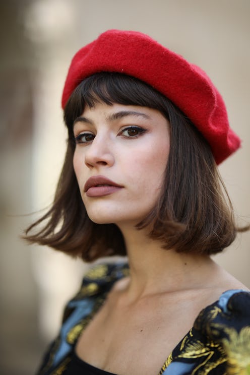 A model posing in a red beret while wearing a floral dress and subtle lipstick