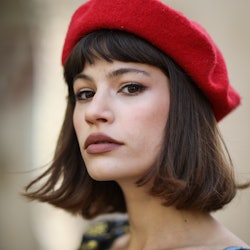 A model posing in a red beret while wearing a floral dress and subtle lipstick