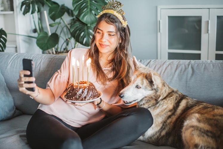 A birthday girl takes a selfie with her dog, while holding some birthday cake with candles. 
