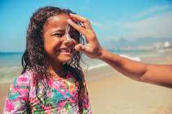 parent putting sunblock on girl's face at beach