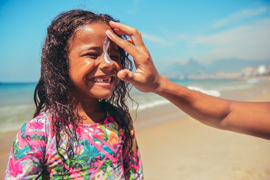 parent putting sunblock on girl's face at beach