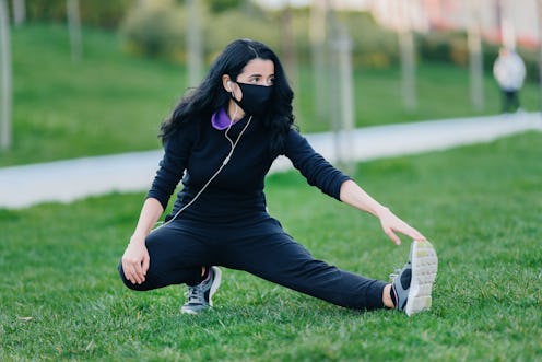A person stretches her hamstring while wearing a mask in a public park. Public parks are starting to...