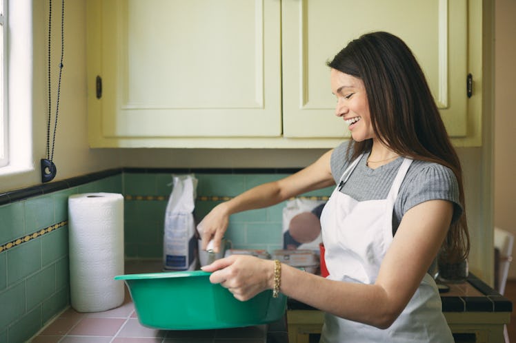 A young woman mixes a cookie dough bread batter in a large, teal bowl in her kitchen.