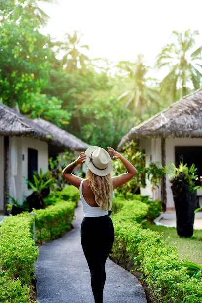 A young woman poses with a group of jungle bungalows on a sunny afternoon.