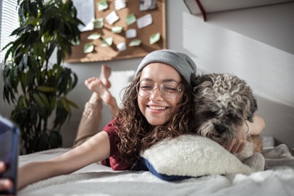 A happy woman hugs her dog, while taking a selfie in bed. 