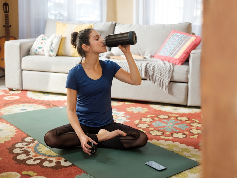 A woman drinks a large nalgene while doing yoga in her living room. Experts explain reasons you're s...