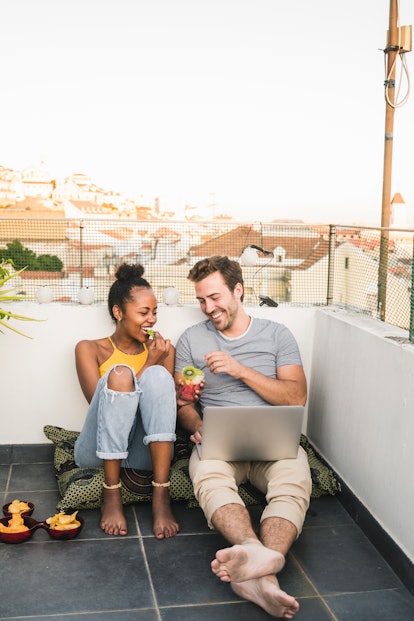 A young couple enjoys snacks and drinks on their rooftop while video chatting.