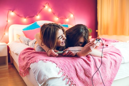 Two girls laugh while laying in bed and playing 'Animal Crossing: New Horizons.'