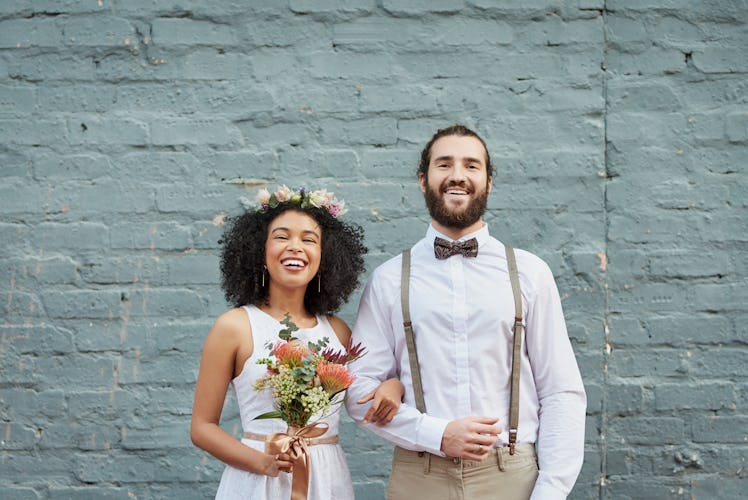 A young couple stands in front of a light blue brick wall on their wedding day.