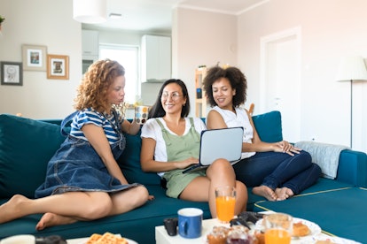 Three young women sit on a blue couch and video chat during a birthday brunch.