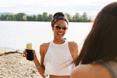 A young woman hangs out on the beach with a drink in her hand, and smiles.
