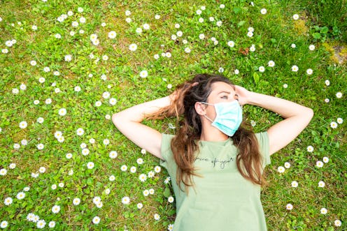A woman lies in a field of flowers wearing a face mask. Face masks can affect your brain in differen...