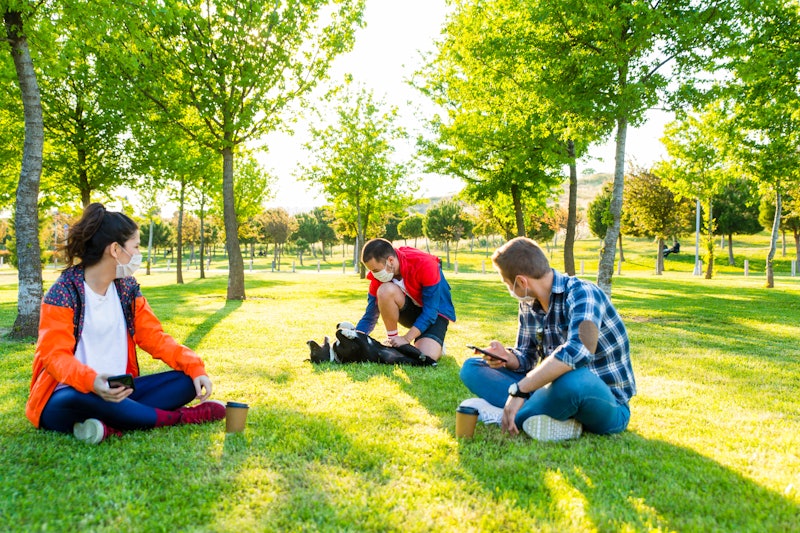 Friends play with their dog in a park. Isolation bubbles of friends or family can be a great way to ...