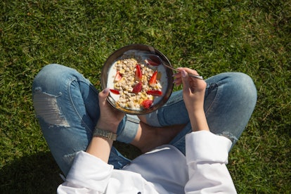 A woman eating yogurt with oats and strawberry slices while sitting on the grass.