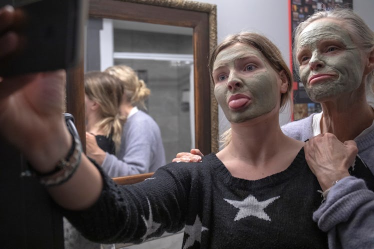 A mother and daughter make silly faces while taking a selfie in face masks.