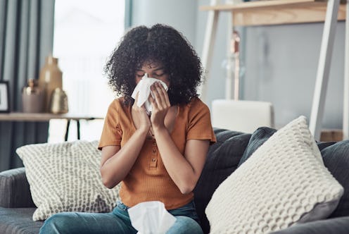 A sick curly-haired girl wiping her nose while sitting on a couch