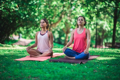 Two women who experience stress and anxiety doing yoga outside on their yoga mats
