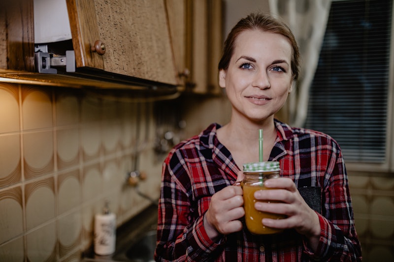A woman wearing a plaid shirt drinking smoothie to help build her immune system