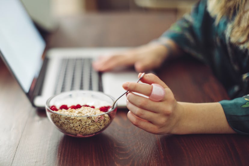 A woman having a yoghurt with cereals and fruit while working on a laptop