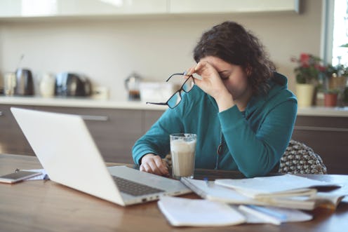 A woman with early signs of lyme disease sitting at her laptop and holding her head in her hand