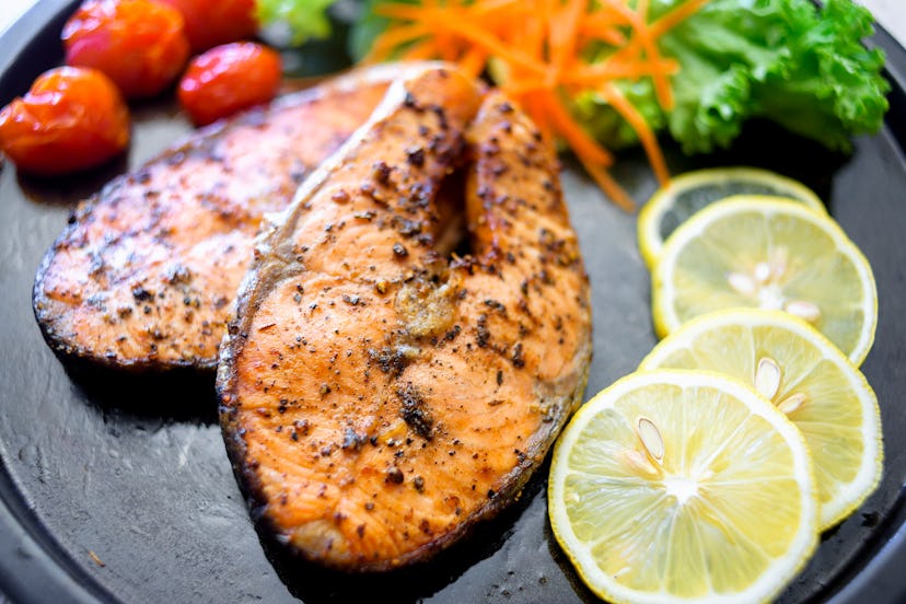 Salmon file full of omega 3's, on a plate with salad, tomatoes and lemon slices