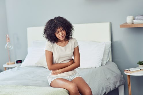 A woman sitting on her bed and holding her stomach with hands due to IBS