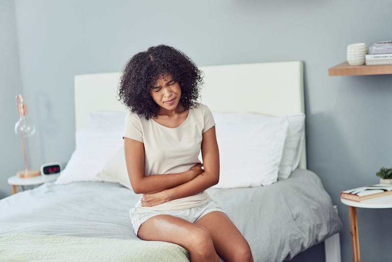 A woman sitting on her bed and holding her stomach with hands due to IBS