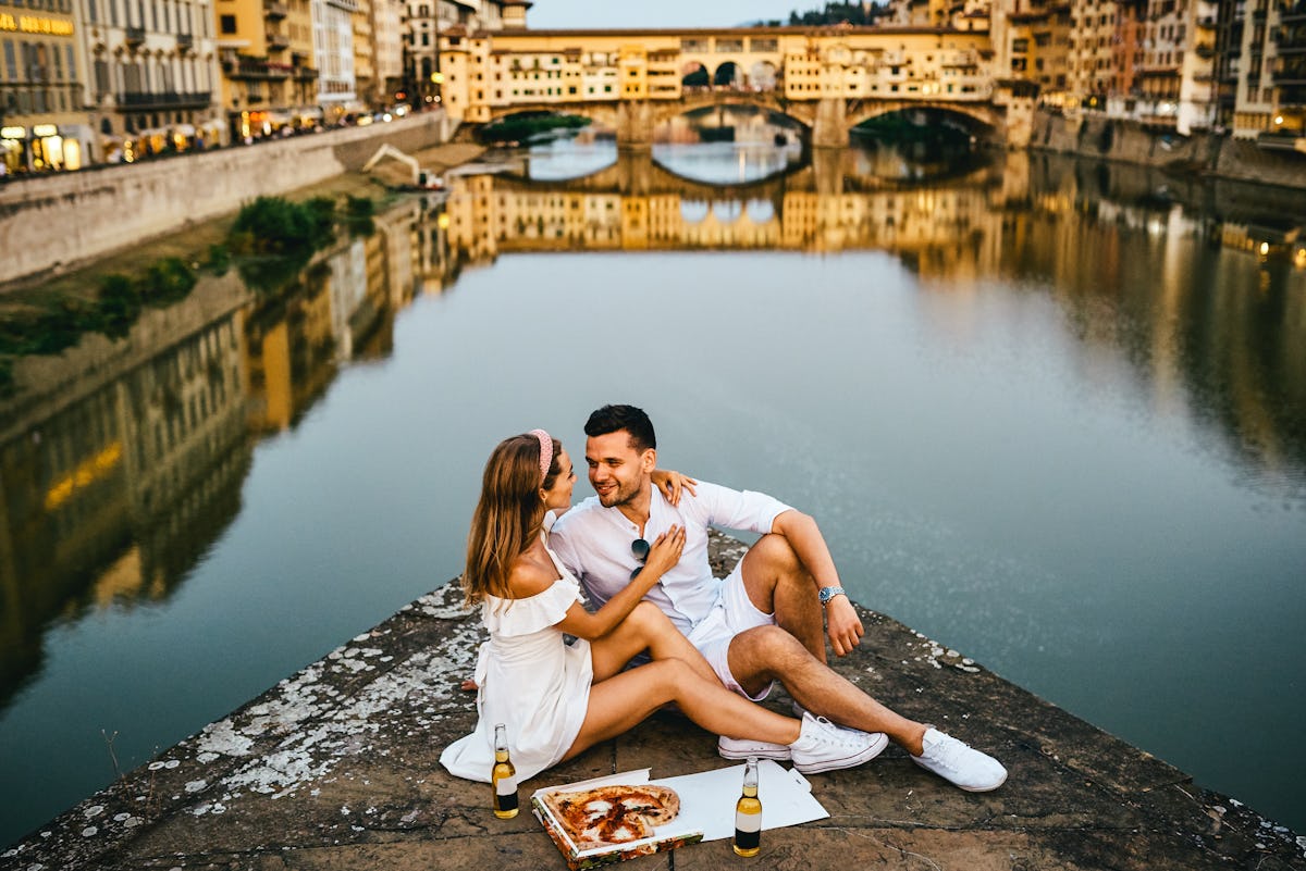 A young couple enjoys pizza and beer while posing for a picture near the Ponte Vecchio in Florence, ...