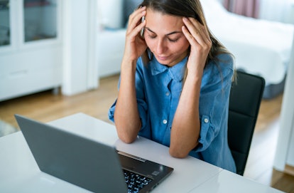 A woman with early signs of lyme disease experiencing a headache while sitting at her laptop