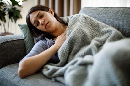 A woman who has Lupus lying on a couch covered with a blanket with her hand on her chest 