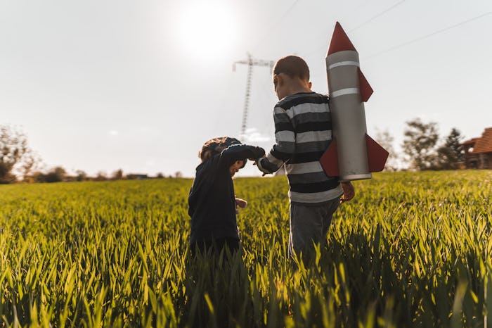 two brothers walking through tall grass with a rocket